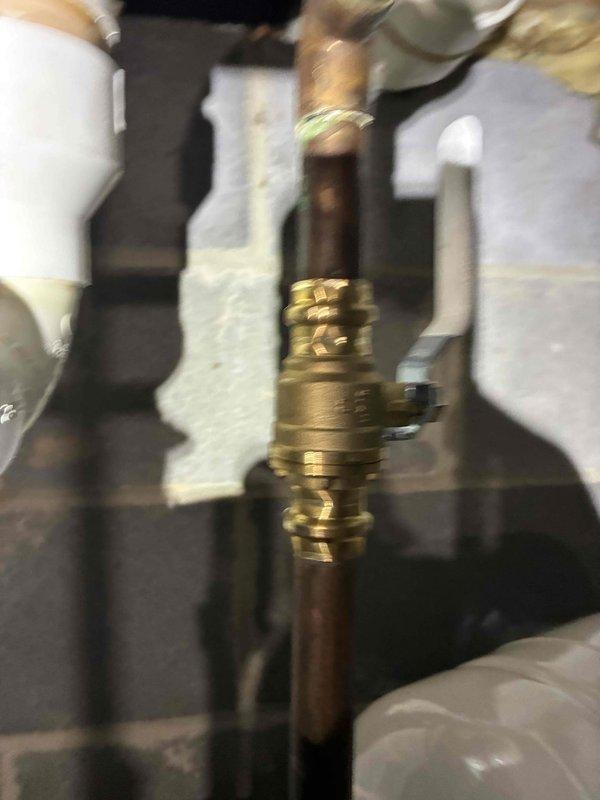 Completed water heater repair service involving the replacement of a faulty valve and installation of an expansion tank to protect the system from thermal expansion pressure. The new brass valve assembly was installed with proper copper pipe connections, and a white expansion tank was mounted and integrated into the plumbing system with appropriate fittings and connectors to ensure optimal performance and code compliance.
