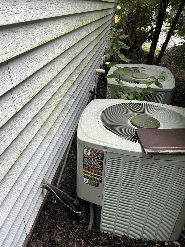 Completed comprehensive HVAC estimate for replacing two existing air conditioning systems with a single zoned system configuration. Evaluated current setup including two outdoor condenser units mounted on exterior wall with weathered siding and existing Goodman furnace in mechanical room, assessed equipment condition and installation requirements for consolidating to one efficient zoned system with appropriate ductwork modifications.