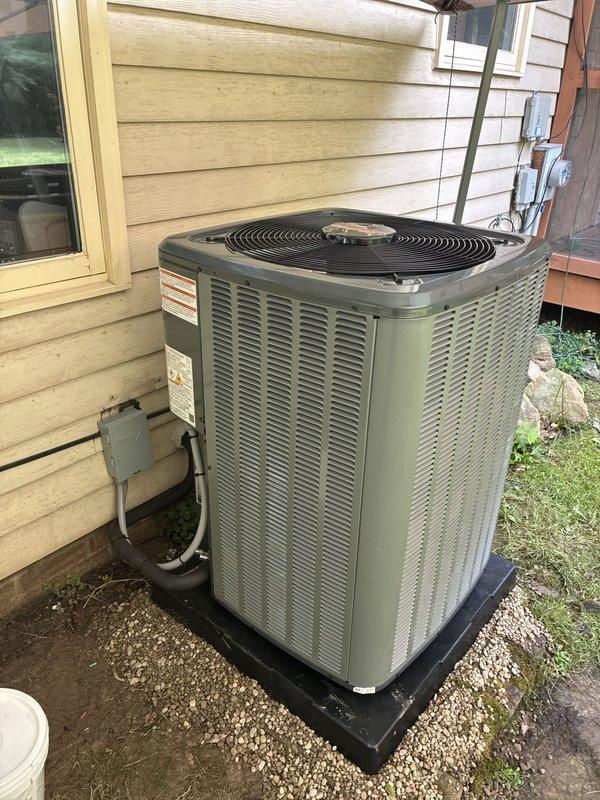 Completed installation of new residential air conditioning system including outdoor condenser unit and associated components. Unit was properly positioned on protective pad with gravel base for drainage, mounted against exterior wall with appropriate clearances, and connected to existing indoor furnace system via refrigerant lines and electrical conduit. All refrigerant connections were secured, system was pressure tested, evacuated, and charged to manufacturer specifications. Verified proper operation of condenser fan, compressor cycling, and airflow through existing ductwork.