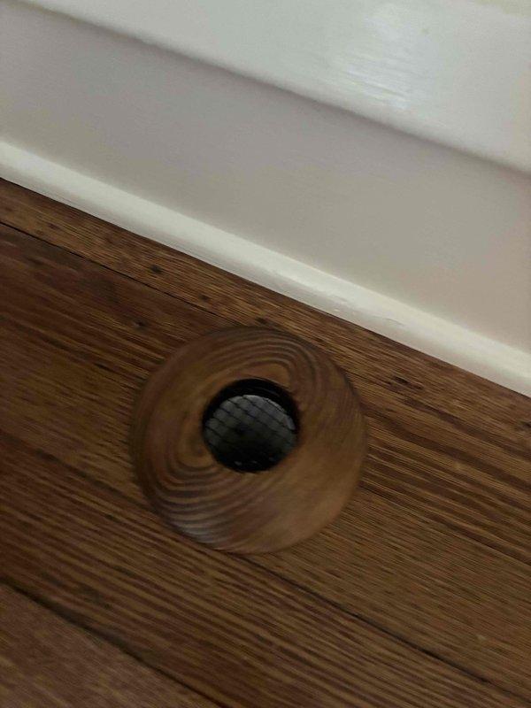 Completed installation of decorative wooden return air vent covers to match existing hardwood flooring and cabinetry. Installed floor register with concentric wooden ring design and central mesh grate, along with cabinet-mounted return air cover featuring natural wood grain finish and circular pull opening, ensuring proper airflow while maintaining aesthetic consistency throughout the space.