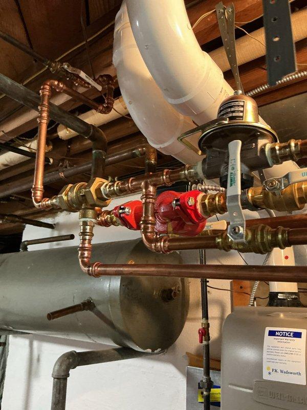 Responded to service call for leaking boiler piping in the afternoon. Upon inspection, identified active leak at copper piping connections near the boiler system. Assessed the piping assembly, including the pressure reducing valve, shut-off valves, and associated fittings mounted to the ceiling joists. Documented existing system configuration showing copper pipe network with brass fittings, expansion tank, and related components. Verified thermostat operation and current system status during diagnostic evaluation.