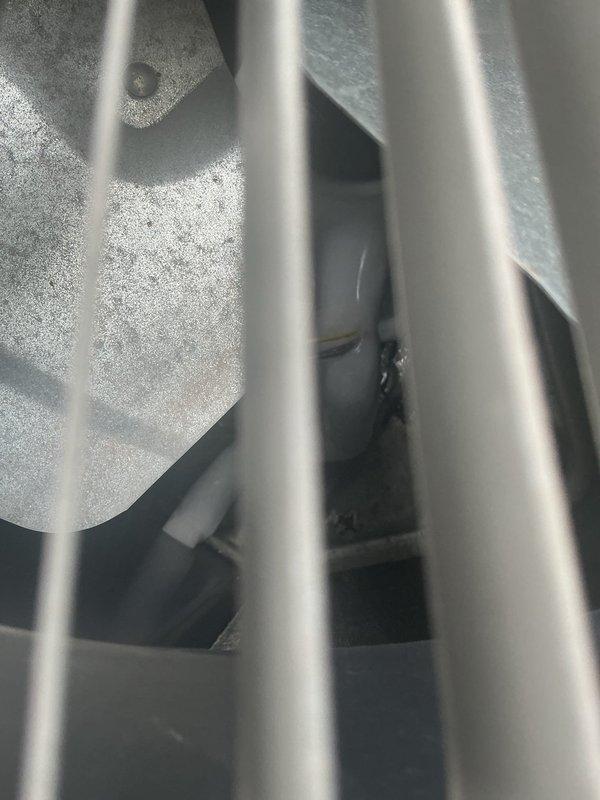 Responded to service call for air conditioning system with flashing green indicator light and frozen evaporator coil. Upon arrival, confirmed extensive frost and ice accumulation on evaporator coil fins and refrigerant lines. Inspected outdoor condensing unit and found refrigerant line connections and drainage components. Documented ice buildup on internal coil surfaces visible through heat exchanger fins, indicating restricted airflow or potential refrigerant flow issues causing coil to operate below freezing temperatures.