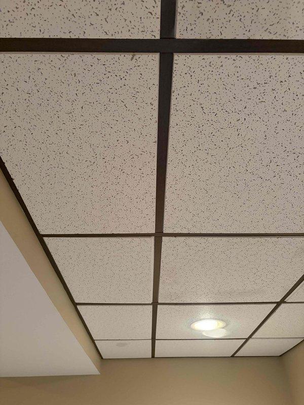 Completed quality check inspection of HVAC system and surrounding ceiling infrastructure. Documented ceiling conditions including exposed plenum area with visible wiring runs, acoustic tile configuration, water staining on ceiling tiles, and LED lighting fixtures. Photographed current system status for record-keeping purposes.