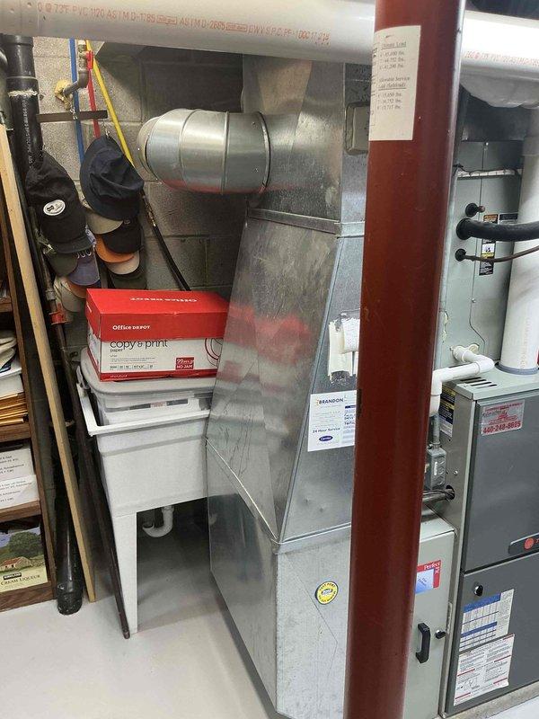 Conducted comprehensive evaluation of 19-year-old residential HVAC system for replacement estimate, including outdoor air conditioning unit and basement furnace installation. Documented existing equipment conditions through photographic assessment, noting exterior condenser placement against property siding and complete basement mechanical room setup with furnace, air handler, and associated ductwork and plumbing connections.