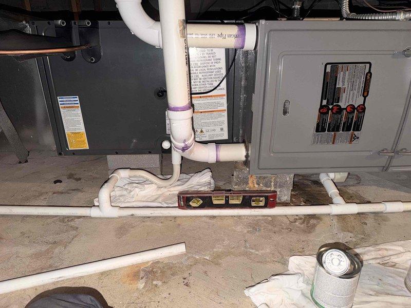 Responded to failed inspection for HVAC installation where condensate line was found to have improper pitch. Documented existing conditions with photographs showing white PVC condensate piping with insufficient slope for proper drainage. Work area included furnace/air handler unit with associated plumbing and electrical components in basement mechanical room, with installation materials and tools visible during assessment.