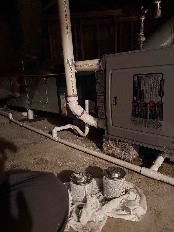 Responded to failed inspection for HVAC installation where condensate line was found to have improper pitch. Documented existing conditions with photographs showing white PVC condensate piping with insufficient slope for proper drainage. Work area included furnace/air handler unit with associated plumbing and electrical components in basement mechanical room, with installation materials and tools visible during assessment.