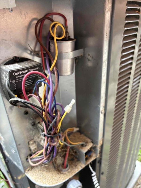 Completed preventive maintenance inspection on residential cooling system. Accessed outdoor condensing unit, inspected electrical components including capacitor and CoreSense diagnostic module with associated wiring connections. Observed normal dirt and debris accumulation on base panel and interior surfaces consistent with regular operation. Inspected condenser coil fins for proper condition and airflow. Checked supply vent grill showing typical wear and minor surface oxidation. All components found operational within normal parameters for ongoing seasonal maintenance program.