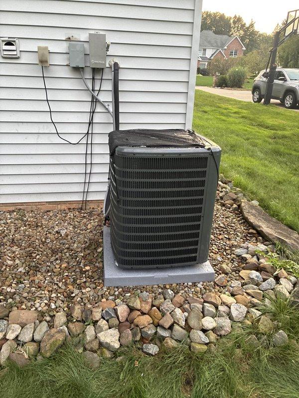 Completed full HVAC air conditioning system installation including outdoor condenser unit mounted on concrete pad with proper gravel bed landscaping and indoor air handler with associated ductwork and PVC condensate drainage in basement utility area. Installed electrical disconnect box on exterior wall with proper conduit and wiring connections, verified all refrigerant lines properly insulated and secured, and confirmed system operational with appropriate airflow and cooling capacity.