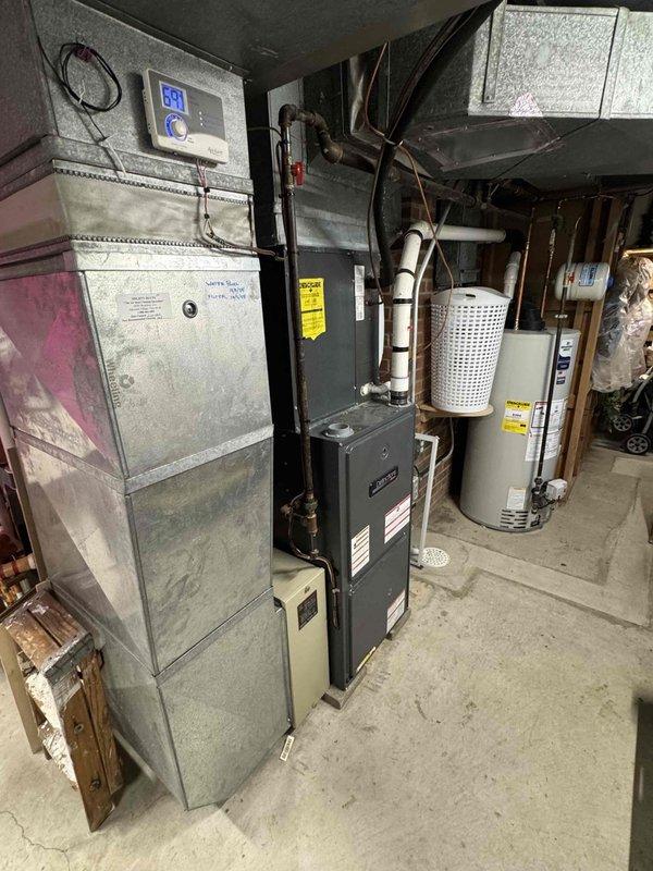 Responded to no cooling complaint on residential air conditioning system. Upon arrival, accessed basement mechanical room and performed diagnostic testing of HVAC equipment. Utilized digital multimeter to check electrical components and verify proper voltage and amperage readings at the air handler unit. Inspected furnace/air handler assembly, refrigerant lines, and associated electrical connections. Documented equipment conditions with photos showing overall system configuration including furnace unit with control panel, air handler with refrigerant line connections, and general mechanical room layout. Performed electrical diagnostics at component level to identify cause of cooling failure.