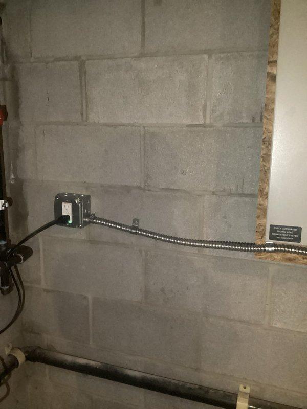 Installed dedicated electrical outlet for tankless hot water heater in utility area. Ran flexible metal conduit along concrete block wall from junction box to new heavy-duty outlet box, ensuring proper support and code-compliant installation. Documented completed installation with photographs showing conduit routing, outlet box mounting, and connection points in proximity to existing plumbing infrastructure.