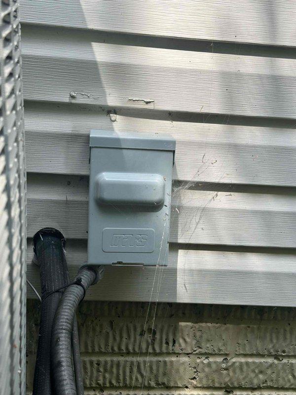 Completed afternoon cooling system tune-up for non-member residential unit. Performed standard maintenance inspection including electrical measurements using clamp meter at outdoor condensing unit, verified proper amperage draw showing 83.0 amps on display. Inspected exterior disconnect box and electrical connections at unit mounted on building foundation, noting weatherproof components in serviceable condition.