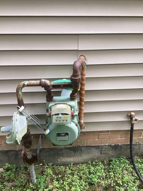 Conducted on-site assessment for residential backup generator installation. Evaluated existing natural gas meter and supply infrastructure, documenting current gas line configuration, meter capacity, and available connection points. Inspected exterior utility access areas and identified optimal placement zones for generator unit considering clearance requirements, fuel source proximity, and electrical service panel accessibility. Photographed gas meter assembly showing copper supply piping with visible oxidation and existing utility connections mounted on vinyl-sided structure with brick foundation. Assessed yard conditions and documented available space for generator pad installation and necessary utility routing.