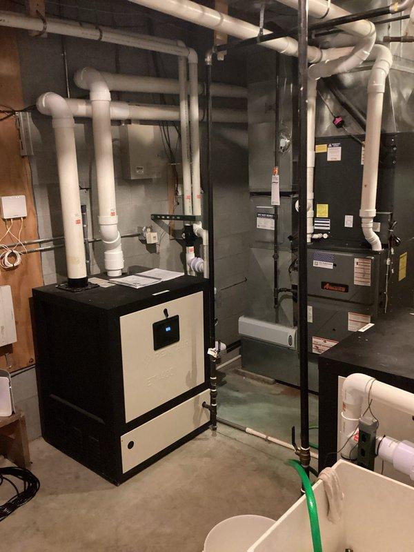 Completed installation of PVC elbows and intake screens on heating equipment in basement mechanical room. Documented existing HVAC system configuration including boiler unit with digital display and furnace with associated white PVC venting system. Obtained measurements of the installation area and captured detailed photographs of the mechanical space for combustion air calculation requirements. The work involved routing white PVC piping with multiple elbow joints along concrete block walls, ensuring proper venting configuration for the heating system. Verified all pipe connections and fittings were secure and properly aligned with existing equipment layout.