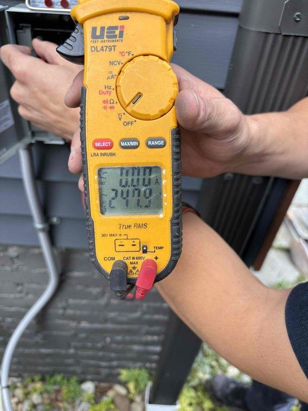Completed mini split system installation with final electrical verification and testing. Performed voltage and amperage measurements using calibration-grade multimeter, confirming system operation at 100.04V supply with proper current draw of 27.10A. Routed line set and electrical connections across flooring area to outdoor condenser unit, ensuring proper system commissioning and full operational status.