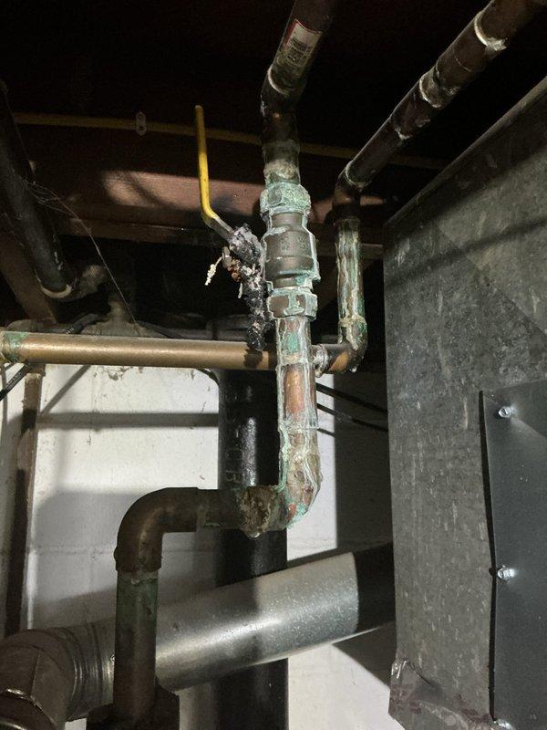 Conducted comprehensive assessment of existing tanked water heater installation showing significant age-related deterioration. Inspected corroded copper supply piping with visible green patina oxidation, multiple threaded fittings, and compromised connections requiring attention. Evaluated water heater tank condition, noting extensive rust and corrosion around top rim and metal surfaces, indicating advanced deterioration. Documented all plumbing connections, including galvanized vertical piping, insulated hot and cold water lines, and pressure relief valve assembly. Photographed existing infrastructure including exposed mechanical systems, ductwork, and structural components for estimate preparation. Provided detailed assessment and recommendations for water heater replacement due to age-related wear and corrosion concerns.