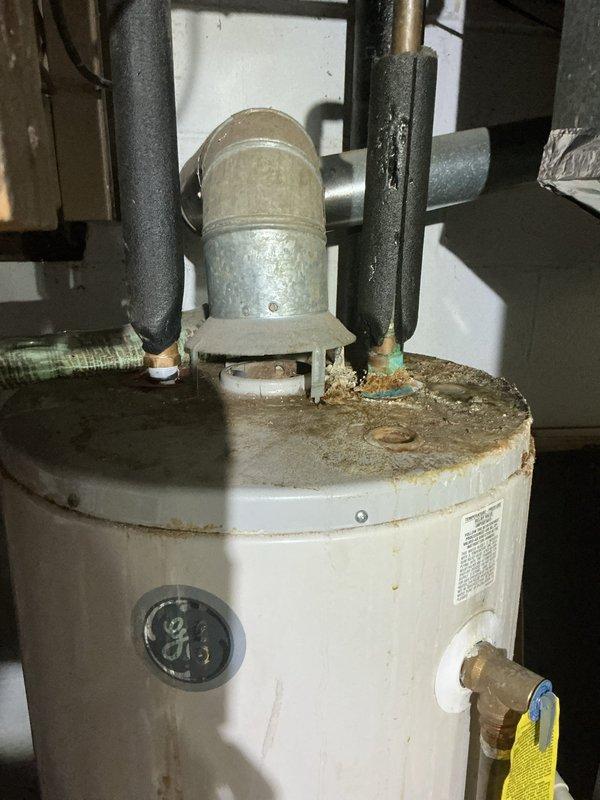 Conducted comprehensive assessment of existing tanked water heater installation showing significant age-related deterioration. Inspected corroded copper supply piping with visible green patina oxidation, multiple threaded fittings, and compromised connections requiring attention. Evaluated water heater tank condition, noting extensive rust and corrosion around top rim and metal surfaces, indicating advanced deterioration. Documented all plumbing connections, including galvanized vertical piping, insulated hot and cold water lines, and pressure relief valve assembly. Photographed existing infrastructure including exposed mechanical systems, ductwork, and structural components for estimate preparation. Provided detailed assessment and recommendations for water heater replacement due to age-related wear and corrosion concerns.