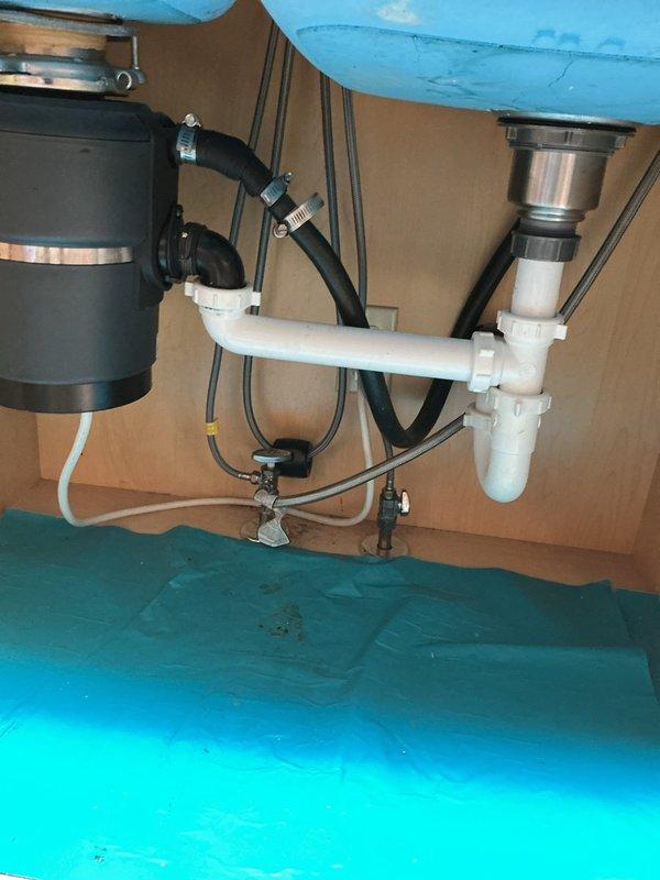 Completed courtesy inspection of kitchen plumbing system including double-basin sink, garbage disposal unit, and drainage assembly. Inspected sink faucet operation and verified proper function of all components. Examined under-sink plumbing configuration consisting of black garbage disposal with connected hoses and metal clamps, white PVC P-trap assembly, and dual drain system with stainless steel strainer basket. All connections, hoses, and clamps were found to be secure with no visible leaks or damage. Also inspected hot water heater per customer request and confirmed proper operation.
