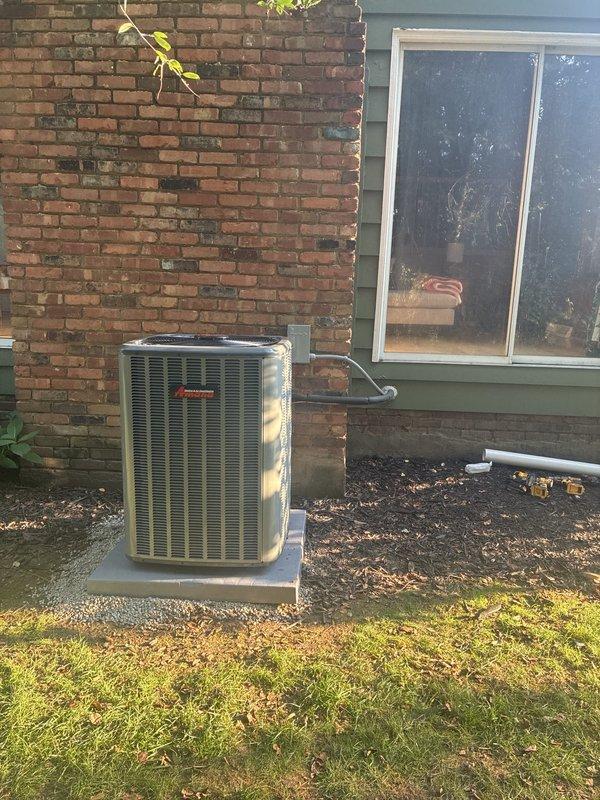 Completed full HVAC system installation including 96% efficiency furnace, air conditioning condenser unit, and whole-home humidifier. New Amana outdoor condenser unit installed on level concrete pad with proper refrigerant line penetration through building exterior, ensuring optimal airflow clearances and stable mounting per manufacturer specifications.