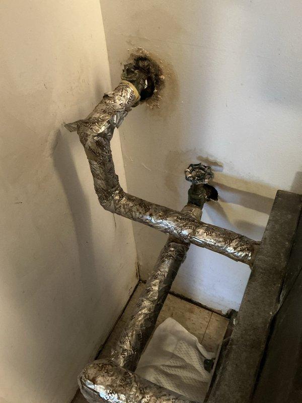 Assessed existing through-the-wall hydronic fan coil unit in condo showing extensive corrosion and active leaking, with no visible manufacturer markings or model identification. Documented current two-wire thermostat configuration connected to building's central boiler system for heating and cooling switchover. Provided replacement equipment recommendations and thermostat compatibility options for the hydronic system, including photographic documentation of deteriorated piping, water-damaged wall surfaces, and existing control wiring for estimate preparation.