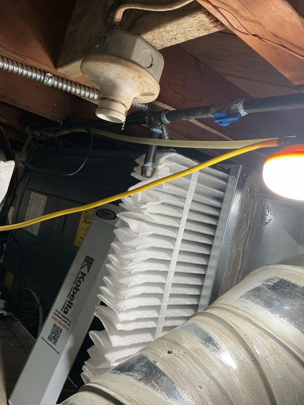 Responded to service call for non-operational air conditioning system affecting entire residence. Upon arrival, inspected five-year-old outdoor condensing unit positioned against exterior brick wall and accessed indoor air handling components in attic space. Performed diagnostic evaluation of system including visual inspection of condenser unit, electrical connections at disconnect box, and indoor air handler with filtration system. Utilized portable lighting to assess attic-mounted equipment and ductwork connections. Documented equipment condition and system configuration through photographic records showing outdoor unit installation with proper clearances and indoor mechanical components including air handler, flexible ductwork, and ventilation grille. Verified system age and configuration matched service records for residential split-system air conditioning unit.