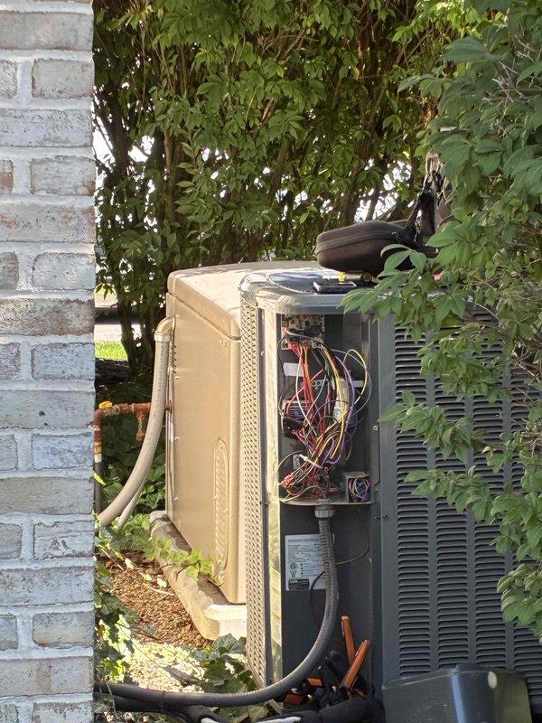 Responded to service call for non-operational air conditioning unit serving bonus room. Upon arrival, located outdoor condenser unit heavily obscured by overgrown vegetation against building exterior. Accessed electrical compartment and inspected control wiring, connections, and internal components. Documented unit condition with equipment age unknown, while two other AC systems on property remained fully functional.