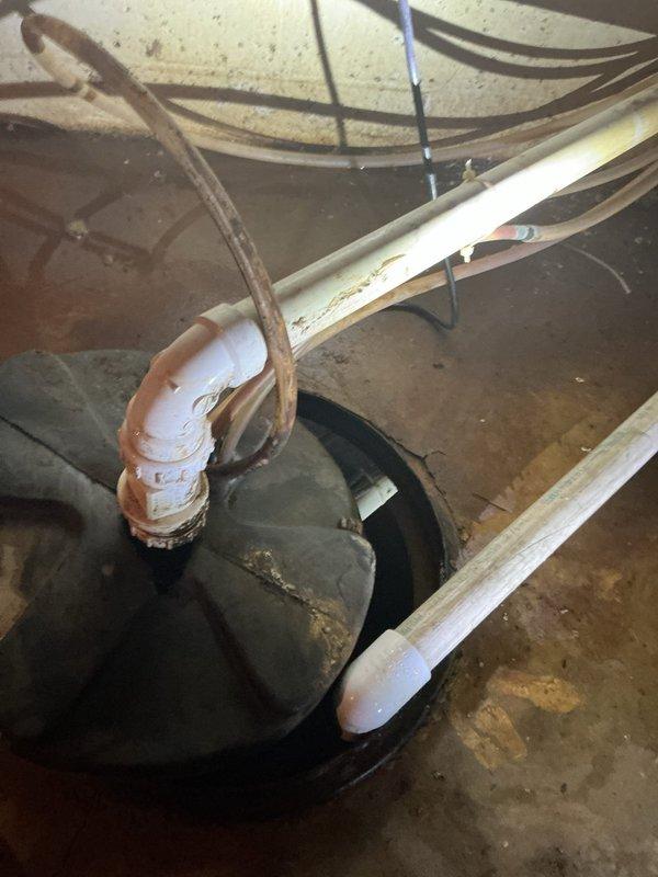 Conducted comprehensive sump pump replacement estimate for failed unit in basement installation. Assessed existing system including corroded copper discharge piping with significant oxidation at elbow joint, PVC vertical discharge pipe, and basin configuration with standing water present. Documented complete failure of current pump and evaluated discharge line condition showing advanced deterioration requiring replacement alongside pump unit.