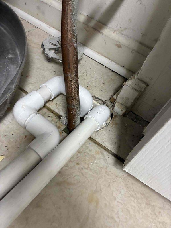 Rerouted water heater pan drain line using white PVC piping with proper elbow fittings to ensure adequate drainage away from the unit. Installed new condensate drainage system on concrete floor to prevent water accumulation in the drip pan beneath the HVAC equipment. All connections were secured and tested to verify proper flow and eliminate potential water damage to the mechanical room.