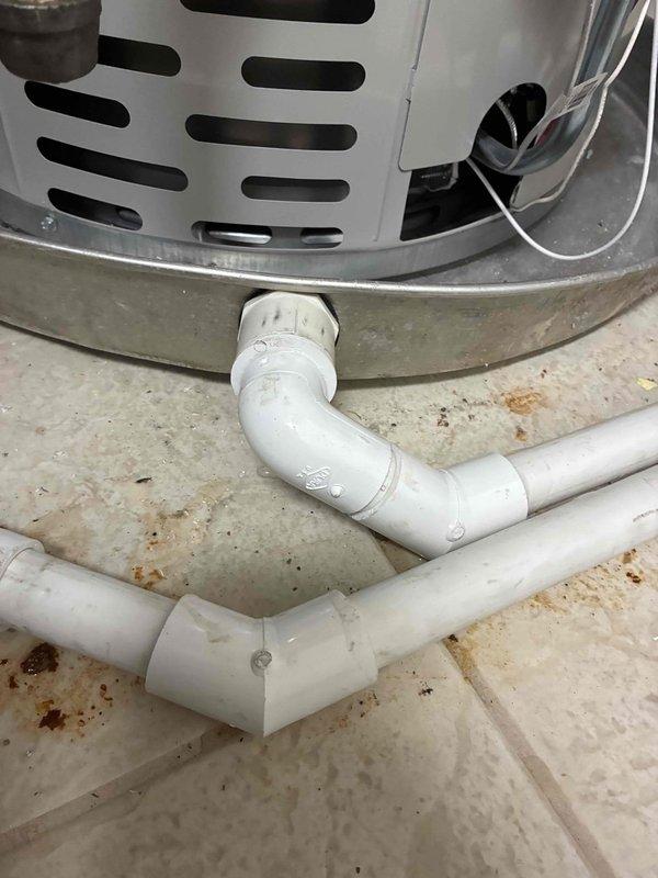 Rerouted water heater pan drain line using white PVC piping with proper elbow fittings to ensure adequate drainage away from the unit. Installed new condensate drainage system on concrete floor to prevent water accumulation in the drip pan beneath the HVAC equipment. All connections were secured and tested to verify proper flow and eliminate potential water damage to the mechanical room.