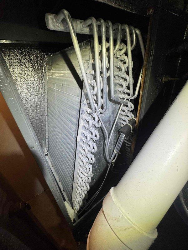 Responded to customer report of furnace leaking extensively. Upon inspection, identified issue originating from evaporator coil assembly and associated condensate drainage system in attic installation. Examined A-coil configuration with serpentine copper refrigerant lines and finned heat exchanger, noting proper coil orientation but potential drainage concerns. Inspected condensate drain lines including PVC piping and connections in confined utility space beneath unit. Assessed drain pan condition, P-trap functionality, and primary/secondary drain line routing. Documented system configuration and leak source with photographic evidence for service records and recommended corrective action to resolve water intrusion issue.