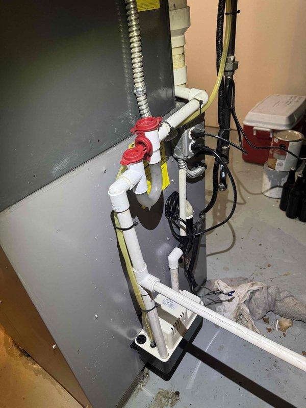 # Condensate Drain Pump Water Leak Repair

Responded to water leak in residential utility area caused by malfunctioning condensate drain pump. Upon arrival, found active water pooling on concrete floor surrounding pump assembly with visible moisture damage on adjacent wall surfaces. 

Diagnosed failed condensate pump unable to properly evacuate water from HVAC system, resulting in overflow condition. Inspected existing white PVC drainage piping configuration with red valve assembly and verified proper downstream drainage pathway. Examined electrical connections and flexible discharge hose for blockages or disconnections.

Replaced defective condensate pump unit with new assembly to restore proper water removal function. Reconnected black flexible discharge hose and white PVC intake piping to new pump housing. Verified pump motor operation and confirmed proper cycling when water level activated float switch. Tested system under load to ensure adequate pumping capacity and no leakage at 