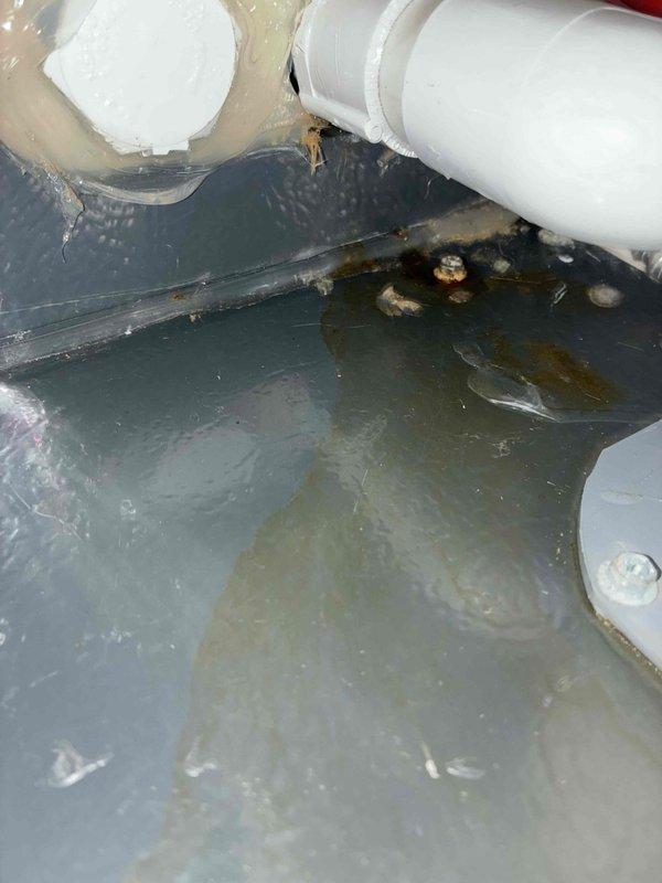 # HVAC Service Call - Water Leakage Investigation

Responded to callback regarding persistent water leakage on top of air conditioning unit following previous day's service visit. Upon arrival, conducted thorough inspection of the system and surrounding area to identify source of continued moisture issue.

Accessed crawl space beneath unit and documented extensive standing water accumulation on waterproof liner throughout the confined area. Multiple puddles with murky, discolored water observed across gray membrane surface, indicating ongoing drainage problem. Inspected overhead PVC drainage pipes and connections for potential leak points or blockages that could be contributing to water presence.

Examined HVAC equipment installation area and photographed refrigerant line set, condensate drain components, and associated piping. Black condensate drain line inspected for proper pitch and flow. Copper refrigerant lines and blue/silver fittings checked for condensation issues. White PVC co