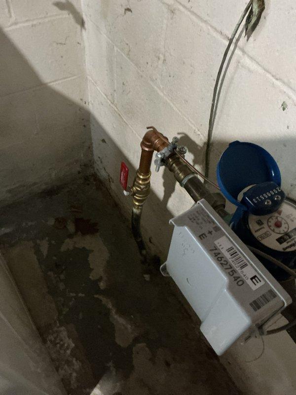 Responded to service call for intermittent swooshing, grunting, and grinding noises originating from water main piping near the shut-off valve assembly. Upon inspection, identified noise source in proximity to the main water meter and shut-off valve, distinct from the water heater system. Documented existing conditions including water meter installation with brass flexible connectors, main supply line configuration, and associated plumbing infrastructure. Evaluated pipe mounting, support systems, and potential causes of hydraulic noise including water hammer, pressure fluctuations, or loose components within the valve assembly. Photographed the water main installation area showing the blue water meter unit, brass fittings, and pipe routing for service documentation. Additionally documented exposed plumbing runs in unfinished wall cavity with visible pipe supports and mounting hardware to assess overall system configuration contributing to noise transmission.