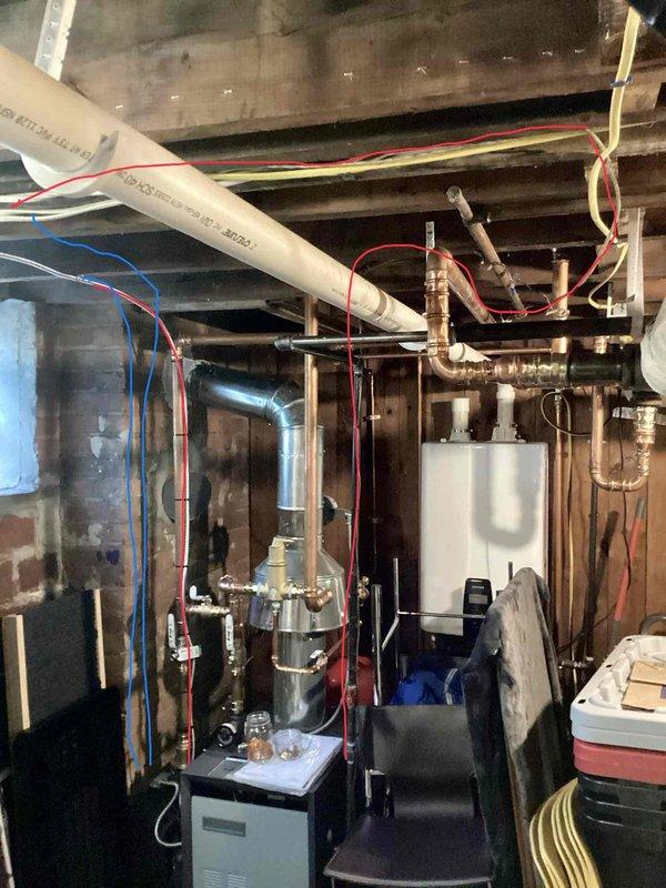 Responded to failed boiler inspection due to critical electrical wiring violations in basement mechanical room. Line voltage wiring was improperly connected to water line, and low voltage wiring was incorrectly attached to gas line, creating serious safety hazards. Documented existing conditions with photographs showing the tankless water heater installation, copper piping network, electrical conduit routing, and control panel configuration to support warranty claim and code compliance requirements.