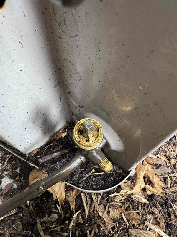 Responded to no cooling complaint on residential air conditioning system. Upon arrival, customer reported lack of cool air and suspected refrigerant leak. Performed visual inspection of outdoor condensing unit and observed signs of refrigerant loss at service valve connections. Identified active leak at brass valve fitting on refrigerant line near ground level, with visible oil residue and debris accumulation indicating prolonged seepage. Documented equipment condition with photographs showing weathered outdoor unit, exposed copper refrigerant lines, and leak point at valve connection. System requires refrigerant leak repair and recharge to restore cooling operation.