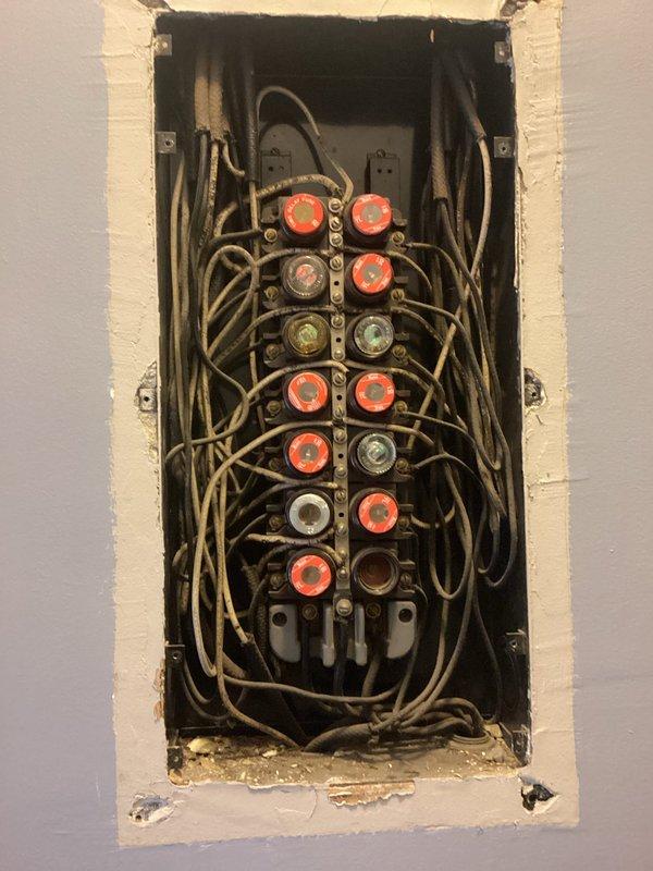 # Electrical Panel and Knob-and-Tube Wiring Assessment

Conducted comprehensive evaluation of existing electrical system requiring complete rewire due to obsolete knob-and-tube wiring throughout the structure. Inspected aging fuse panel with multiple circular fuse holders showing deteriorated condition with disorganized wiring configuration. Documented extensive tan-colored cloth insulation on conductors indicating original installation dating back several decades. Panel exhibited overcrowded wire management with insufficient capacity for modern electrical demands.

Assessed exterior electrical service entry point on brick facade, including meter base installation and existing conduit routing. Evaluated service entrance configuration to determine requirements for new panel replacement and updated electrical distribution system. Photographed current conditions to document scope of work needed for full electrical system modernization including generator installation preparation.

Provide