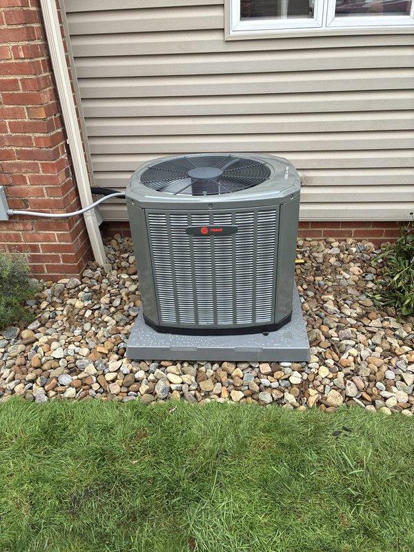 Completed full HVAC system installation including furnace, air conditioning unit, and ductwork liner. Installed Trane brand outdoor condensing unit on concrete pad with proper clearance from structure, positioned on river rock bed for drainage. Unit features protective mesh grilles and fan assembly, mounted against exterior wall with appropriate electrical connections and refrigerant lines. System tested and verified operational upon completion.