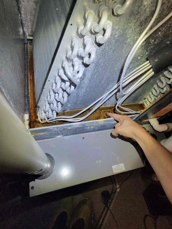 Responded to water accumulation beneath air handler unit in basement. Upon inspection, discovered heavy frost buildup on evaporator coils indicating restricted airflow or low refrigerant charge. Collected standing water from drain pan and documented frozen coil condition with photos for customer records.