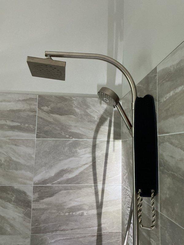 Replaced defective Moen shower cartridge in dual-head shower system featuring rain-style overhead fixture and handheld wand mounted on black vertical panel. Restored proper water temperature control and flow regulation to the modern shower installation with gray marble-patterned tile surround.