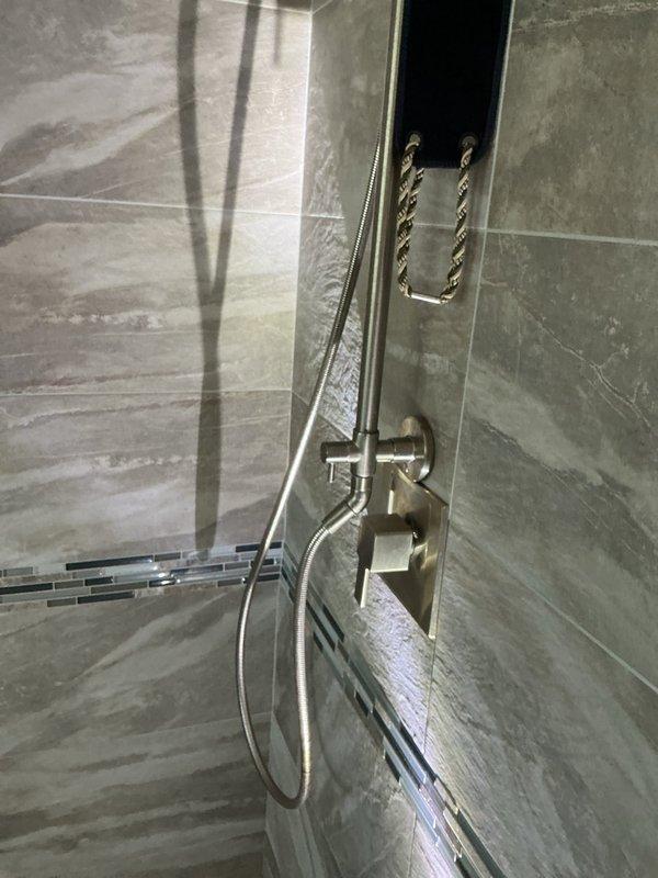 Replaced defective Moen shower cartridge in dual-head shower system featuring rain-style overhead fixture and handheld wand mounted on black vertical panel. Restored proper water temperature control and flow regulation to the modern shower installation with gray marble-patterned tile surround.