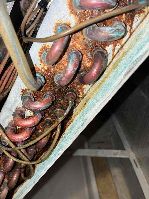 Responded to callback for AC condensate drain issue in laundry room where water continued dripping onto floor following previous service attempt. Upon inspection of 20-year-old air handler unit located in utility closet, found primary drain line remained partially obstructed. Cleared condensate drain line completely using appropriate tools and verified proper flow. Inspected evaporator coil assembly and drain pan for corrosion and debris accumulation. Noted significant rust deterioration on coil housing and mounting components, consistent with age of equipment and prolonged moisture exposure. Verified drain pan integrity and proper pitch for drainage. Flushed secondary drain line to ensure backup system functionality. Tested system operation and confirmed condensate now draining properly with no leakage onto floor. Advised customer of aging equipment condition and potential for future reliability issues given extensive corrosion observed on internal components.