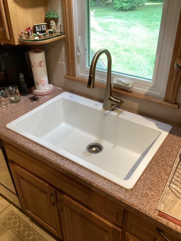 Installed new Moen pull-down kitchen faucet with brushed nickel finish and large white single-basin granite sink with integrated drainboard section in existing countertop opening. Connected all supply lines, drain assembly with P-trap, and verified proper operation of all components with no leaks detected.
