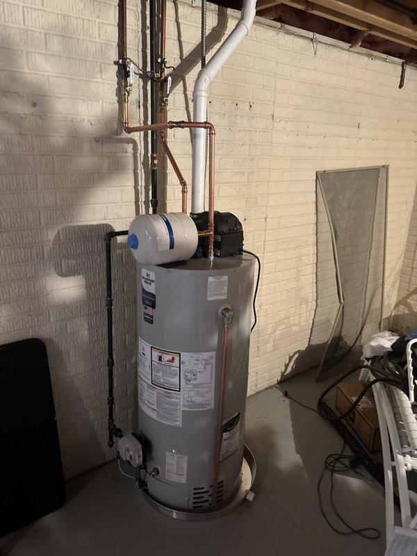 Completed installation of 50-gallon power vent water heater in residential basement utility area. Unit was properly connected with copper supply lines, PVC venting, expansion tank, and circulation pump, with all plumbing connections secured and tested for proper operation. Installation included mounting expansion tank to wall, routing exhaust venting through existing penetration, and verifying all safety labels and manufacturer specifications were visible per code requirements.