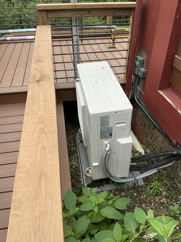Conducted estimate for replacement of 25-year-old non-functional ductless mini-split system including both outdoor condenser unit and indoor air handler. Existing system has failed beyond repair and requires complete replacement. Documented current equipment installation locations, with outdoor unit positioned beneath elevated deck structure and indoor wall-mounted unit installed in living space with exposed brick wall. Assessed electrical connections, refrigerant line routing, and mounting configurations to determine replacement specifications and installation requirements.