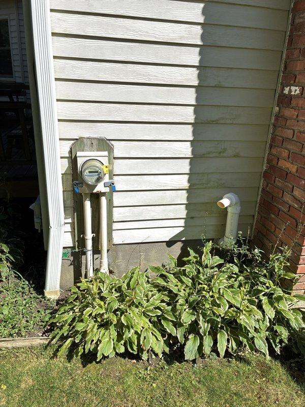 Completed residential HVAC assessment for air conditioning replacement options on a property with a 1992 AC unit and newer furnace. Documented existing outdoor condenser unit with cylindrical mesh cage design, evaluated system age and condition, and photographed current equipment configuration including generator and utility connections for replacement proposal development.