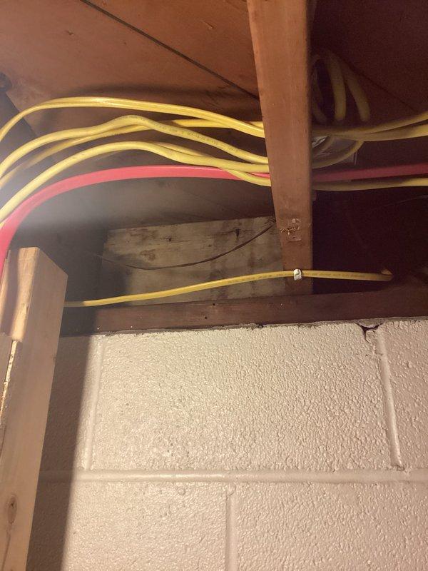 Responded to service call for mini split system displaying red indicator light. Customer reported unit had never been operated since installation, with air discharging from top of unit rather than bottom louvers, and both blue and red lights illuminating. Upon arrival, conducted visual inspection of indoor and outdoor components. Issue was identified during pre-occupancy inspection process. Documented installation deficiencies including unsecured refrigerant line sets requiring proper stapling per code requirements and loose sheet metal fasteners on ductwork connections. Photographed electrical panel installation and exposed mechanical systems in basement area showing bundled wiring routes through ceiling joists and refrigerant lines. Findings will be submitted to permit department to address inspector's noted deficiencies before final approval can be granted.