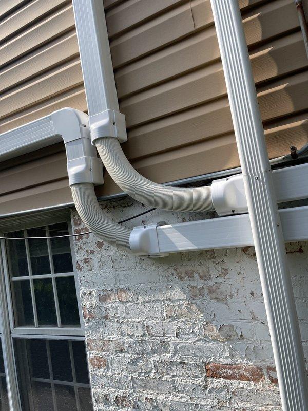 Completed installation of Daikin mini-split air conditioning system on residential property exterior. Mounted outdoor condenser unit on black pad at ground level with proper clearances, ran refrigerant line sets in white PVC covers vertically along building exterior to indoor unit location, and installed electrical conduit and wiring to power the system. All components secured to exterior wall surfaces, system tested and operational upon completion.