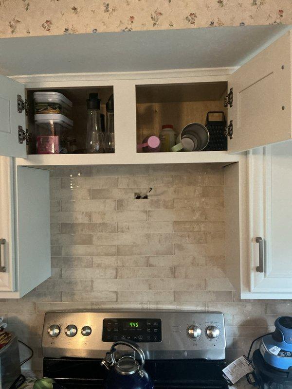 Installed electrical outlet in kitchen backsplash area above countertop near stove range. Outlet was properly positioned within the tiled wall surface to provide convenient access for small appliances while maintaining the aesthetic appearance of the beige and gray tile pattern.