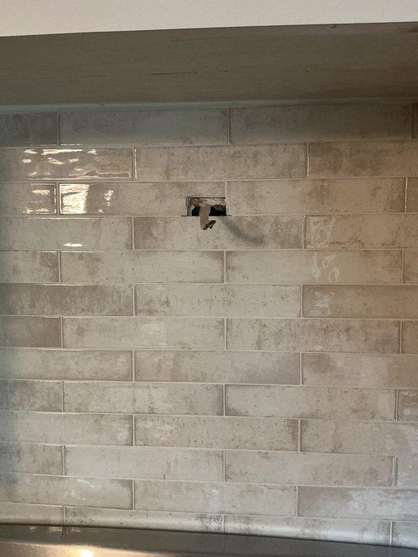 Installed electrical outlet in kitchen backsplash area above countertop near stove range. Outlet was properly positioned within the tiled wall surface to provide convenient access for small appliances while maintaining the aesthetic appearance of the beige and gray tile pattern.