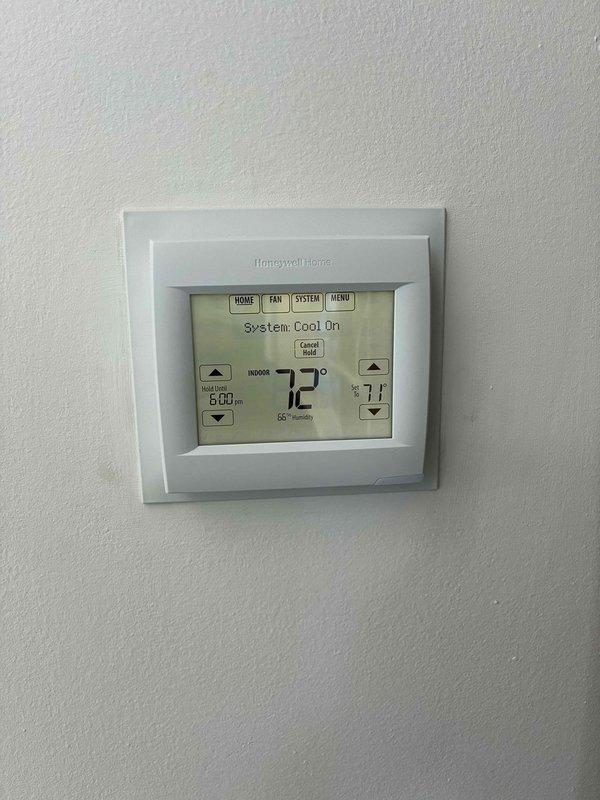 Responded to service call for cracked thermostat that was previously replaced. Removed damaged Honeywell Home digital thermostat unit and installed new replacement unit on existing wall mount. Verified proper system operation with cooling mode engaged, confirmed accurate temperature display reading 72°F, and tested all control functions including temperature adjustment arrows, system settings, and programmable features. System operating normally upon completion.