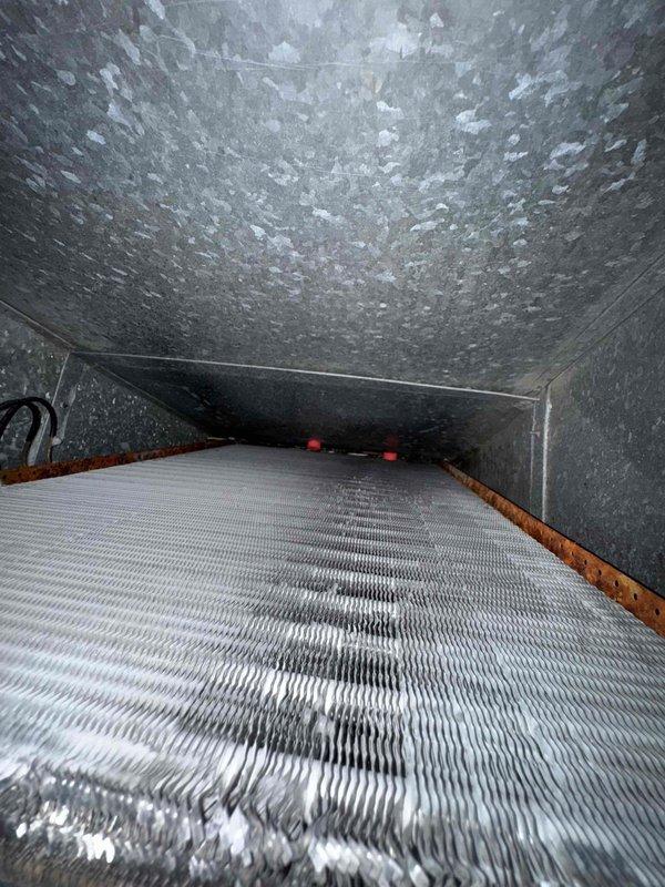 Responded to service call for active water leak originating from furnace blower area in basement. Upon inspection, discovered significant condensate drainage issue caused by corroded evaporator coil and accumulated debris within the ductwork system. The 5-year-old furnace unit exhibited extensive rust staining across the evaporator coil surface, indicating prolonged moisture exposure and inadequate drainage. Interior ductwork inspection revealed heavy dust accumulation, mineral deposits on metal surfaces, and rust-colored staining along bottom seams where water had been pooling. Documented corroded coil condition and contaminated ductwork with photographic evidence for service records. Identified primary cause as compromised coil integrity combined with blocked or insufficient condensate drainage system, resulting in water overflow onto basement floor.